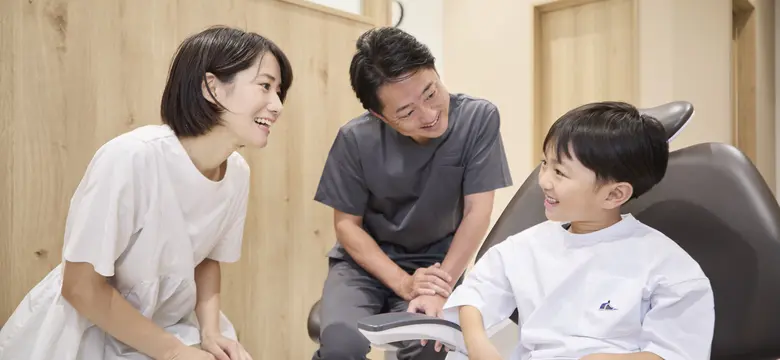 診療チェアのお子さまと保護者に笑顔で話しかける歯科医師